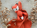 Crocheted fox toy on a red blanket with dried leaves around
