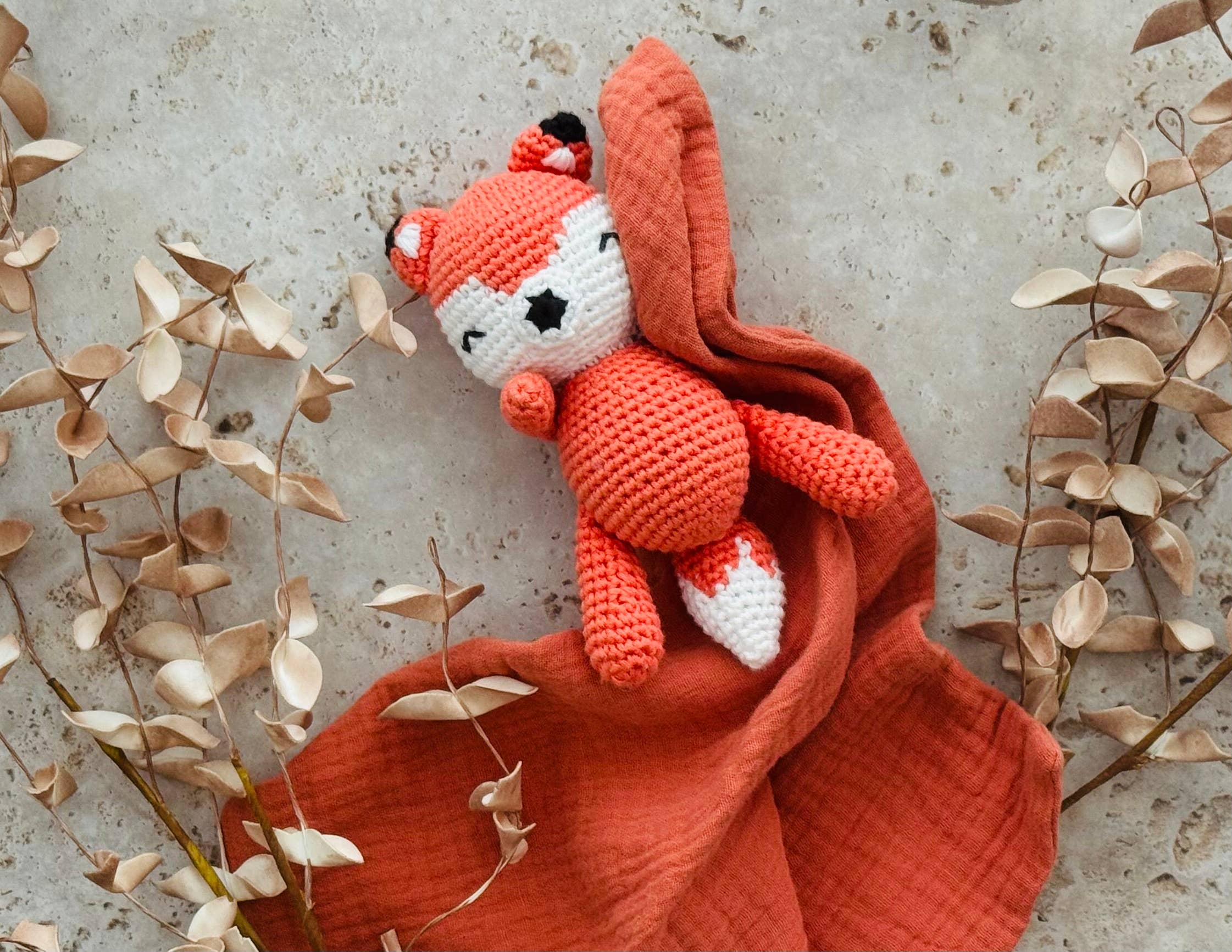 Crocheted fox toy on a red blanket with dried leaves around