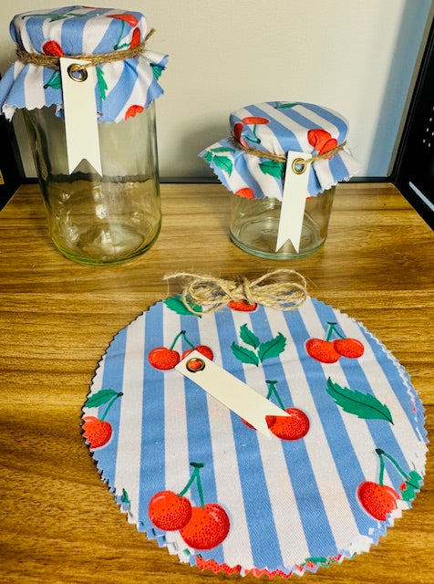 Two jars with fabric covers featuring cherry designs on a wooden surface.