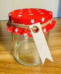 Clear glass jar with a red star-patterned lid and a white tag on a wooden surface.