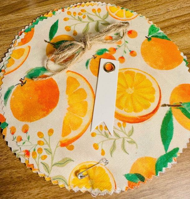 Round fabric swatch with orange and lemon pattern on a wooden surface