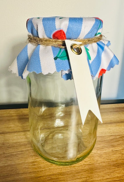 Clear glass jar with a colorful striped lid and decorative tag on a wooden surface.