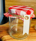 Clear glass jar with a red and white checkered lid and a white tag on a wooden surface.
