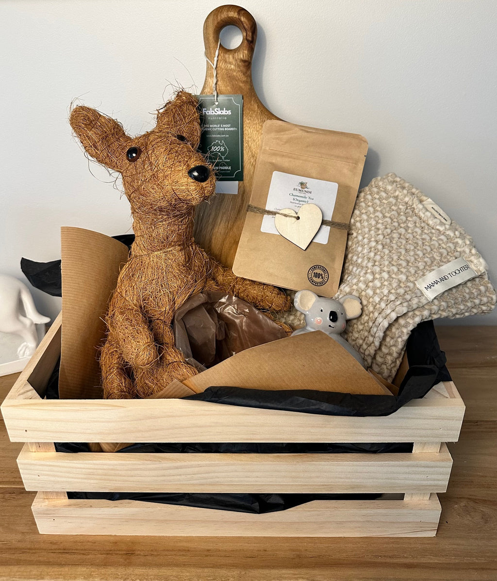 Gift basket with a stuffed animal, coffee package, and blanket on a wooden surface.
