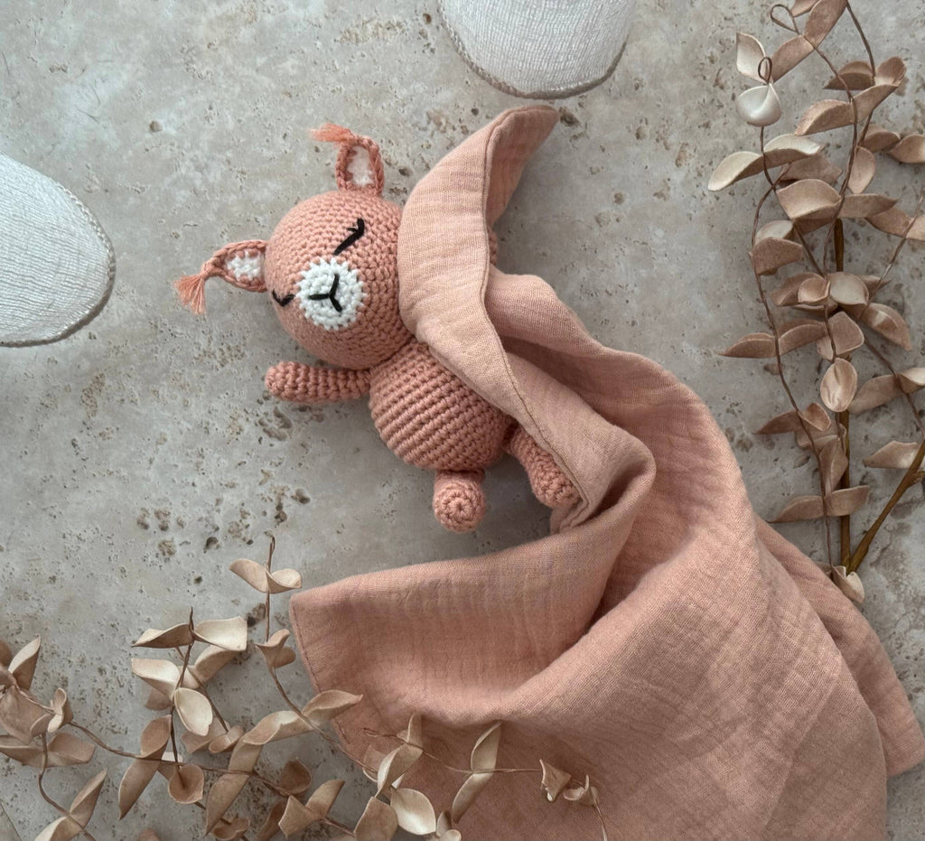 Pink plush toy with a blanket on a textured surface with leaves.