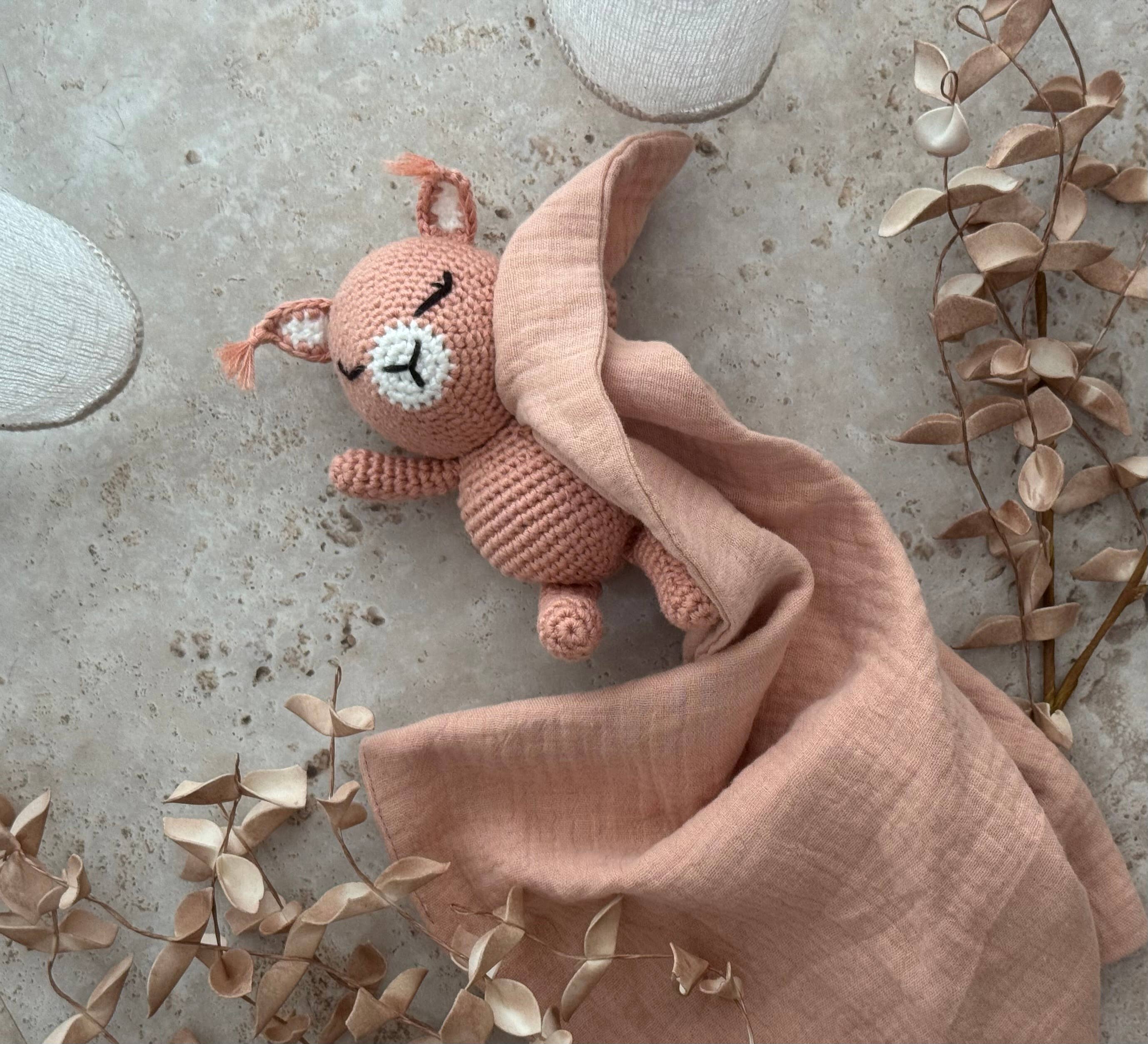 Pink plush toy with a blanket on a textured surface with leaves.