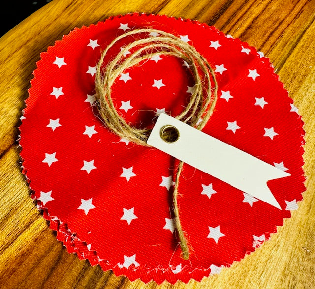 Red circular fabric with white star patterns, twine, and a tag on a wooden surface
