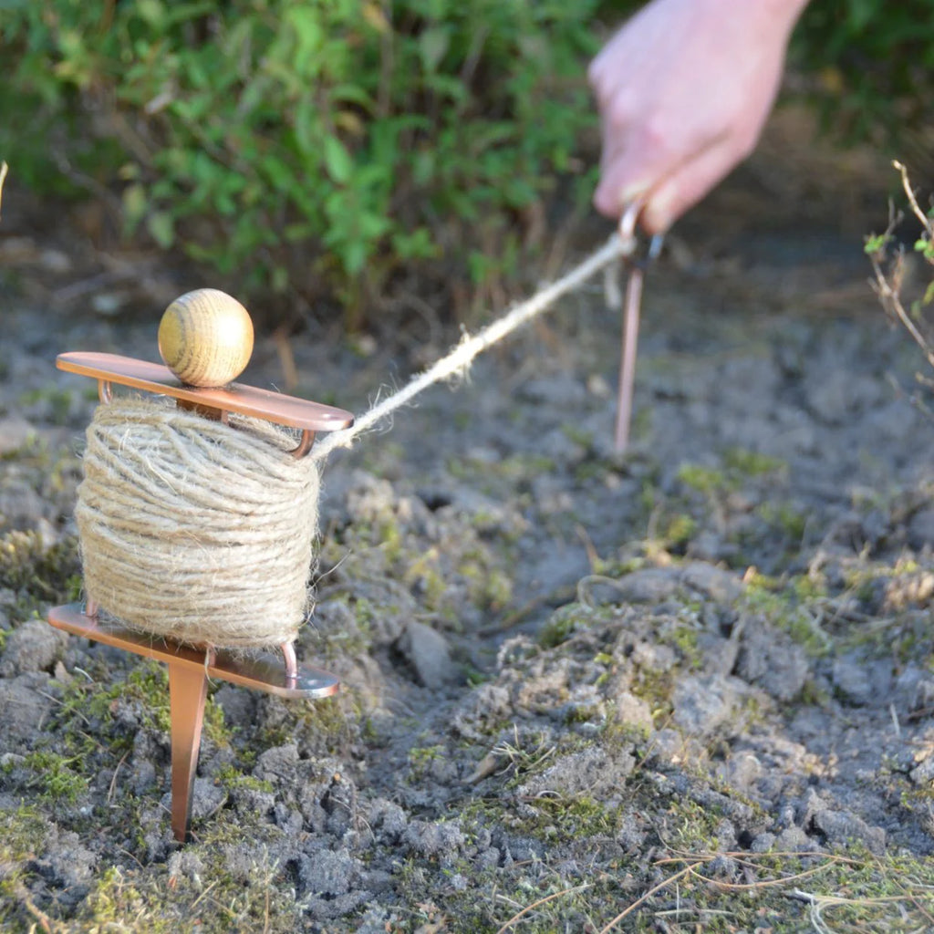Person using a spool of twine on a rocky surface with greenery in the background