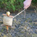 Person using a spool of twine on a rocky surface with greenery in the background