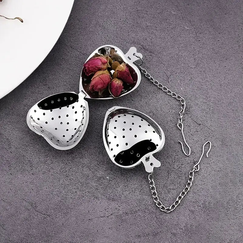 Heart-shaped metal tea infuser with chain on a gray surface