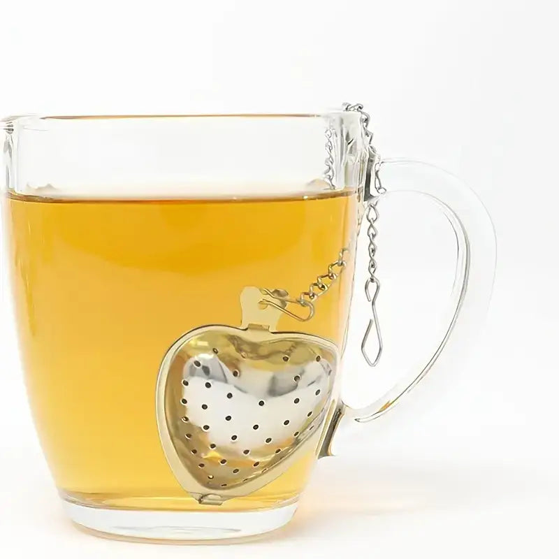 Glass mug with heart-shaped metal tea infuser and yellow liquid on a white background