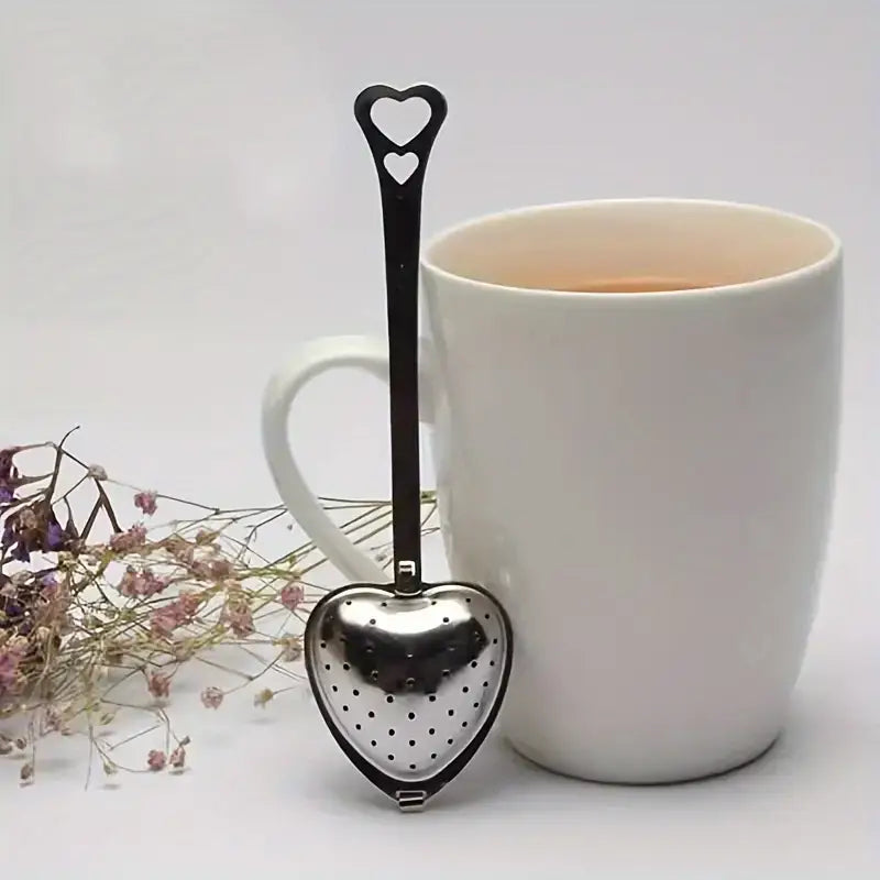 Heart-shaped tea infuser in front of a white mug with tea, on a light background.