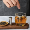 Tea-making process with a glass of tea, tea leaves, and tea infuser on a wooden board.
