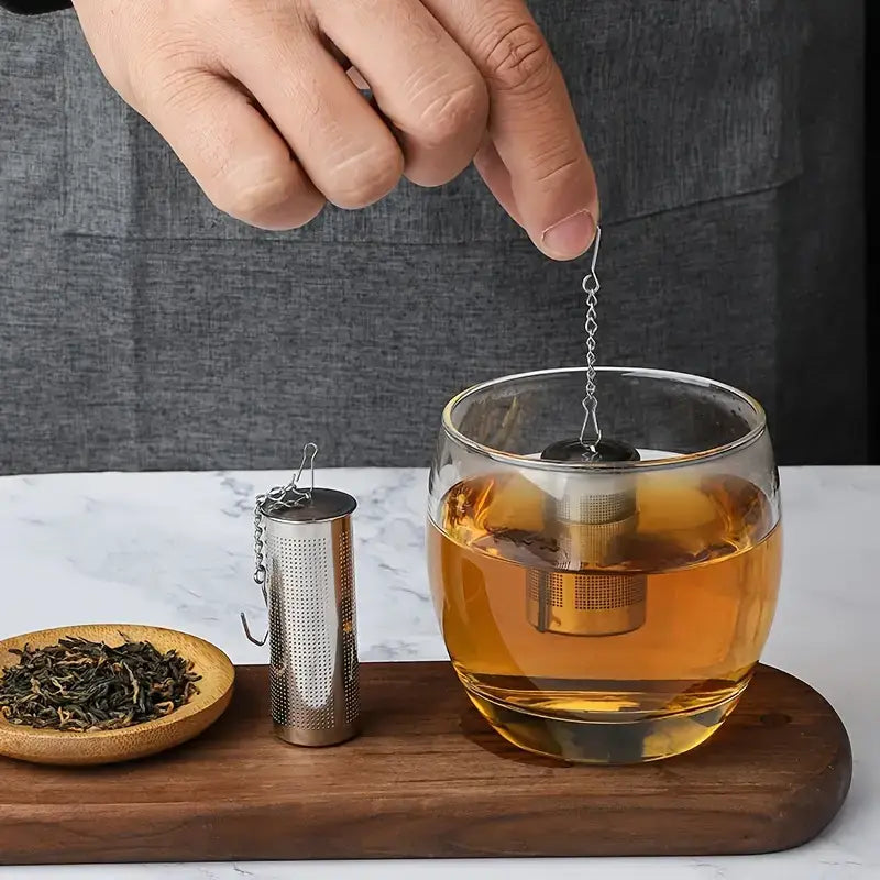 Tea-making process with a glass of tea, tea leaves, and tea infuser on a wooden board.